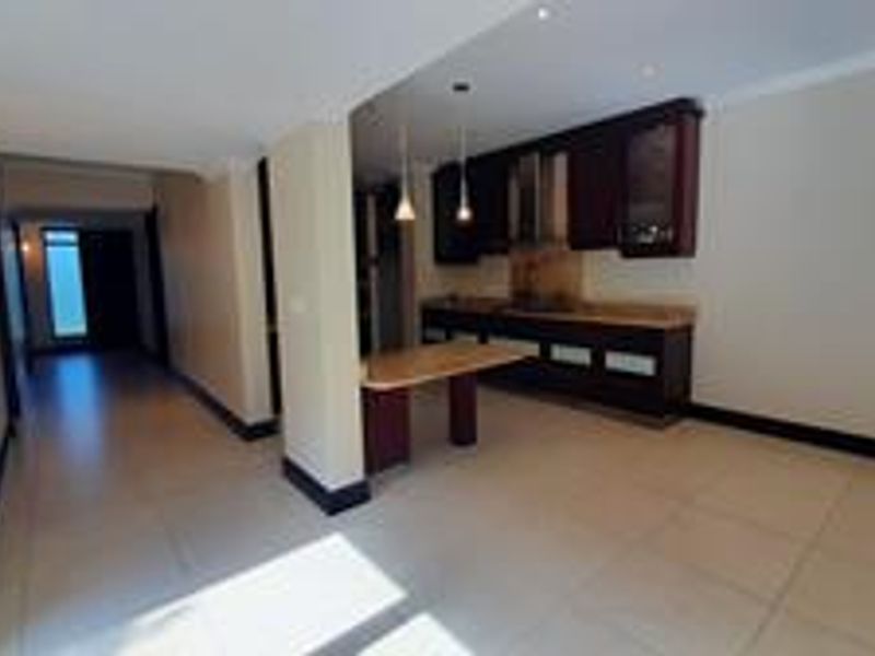 Spacious open-plan living area featuring a modern kitchen with dark cabinetry, built-in appliances, and tiled flooring throughout.