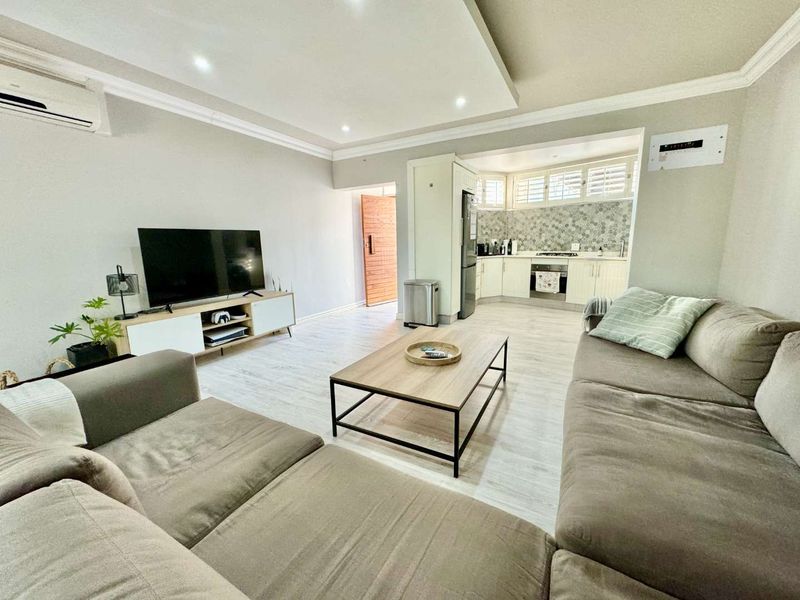 Open-plan living area featuring a modern kitchen with built-in appliances, recessed ceiling lighting, and light-toned laminate flooring throughout the space.