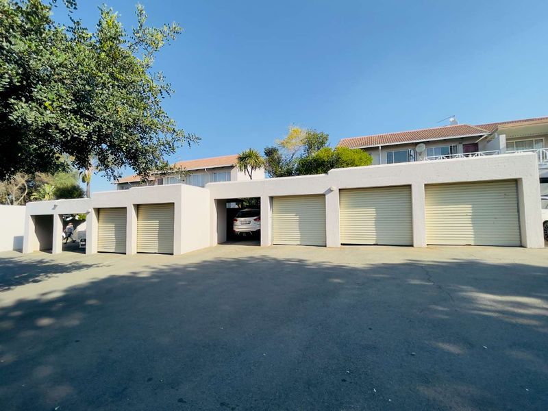A row of multiple garage units with roller shutter doors and an asphalt driveway area in front of the apartment complex.
