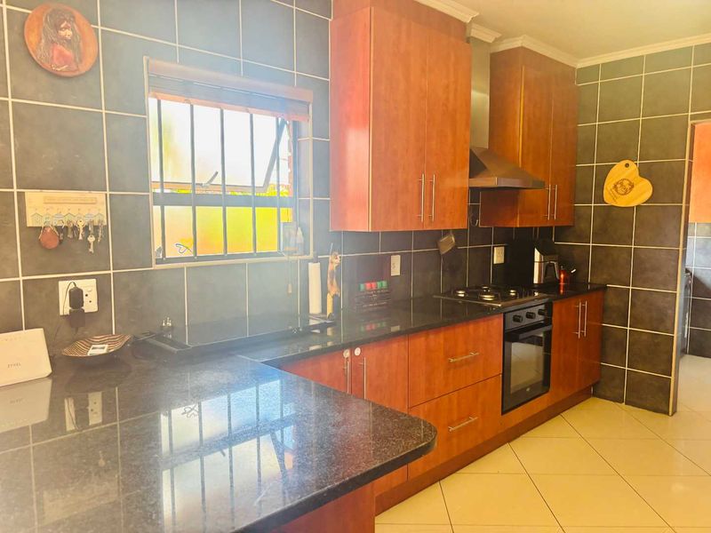 A functional kitchen featuring dark granite countertops, wood-finish cabinetry, a built-in oven with gas hob, and dark tiled wall finishes.