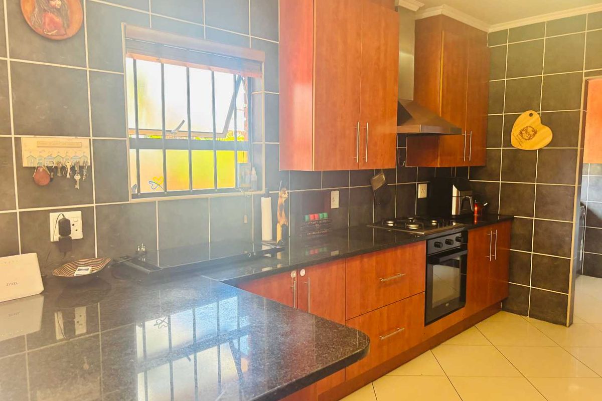 A functional kitchen featuring dark granite countertops, wood-finish cabinetry, a built-in oven with gas hob, and dark tiled wall finishes.