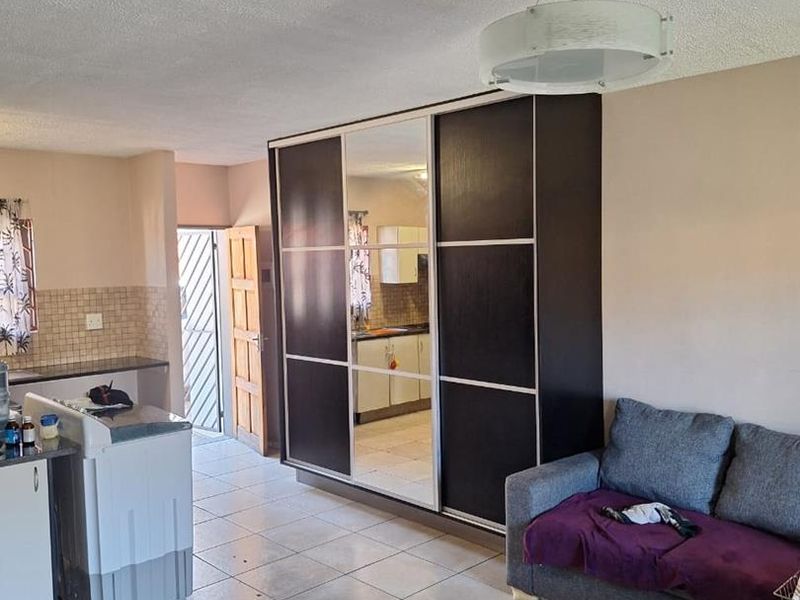 Open plan living area featuring tiled flooring, a large built-in wardrobe with mirrored panels, and an adjacent kitchen space with tiled backsplash.