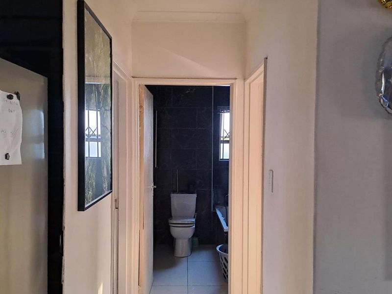 A view through a hallway leading into a bathroom featuring dark wall tiles and a standard flush toilet.