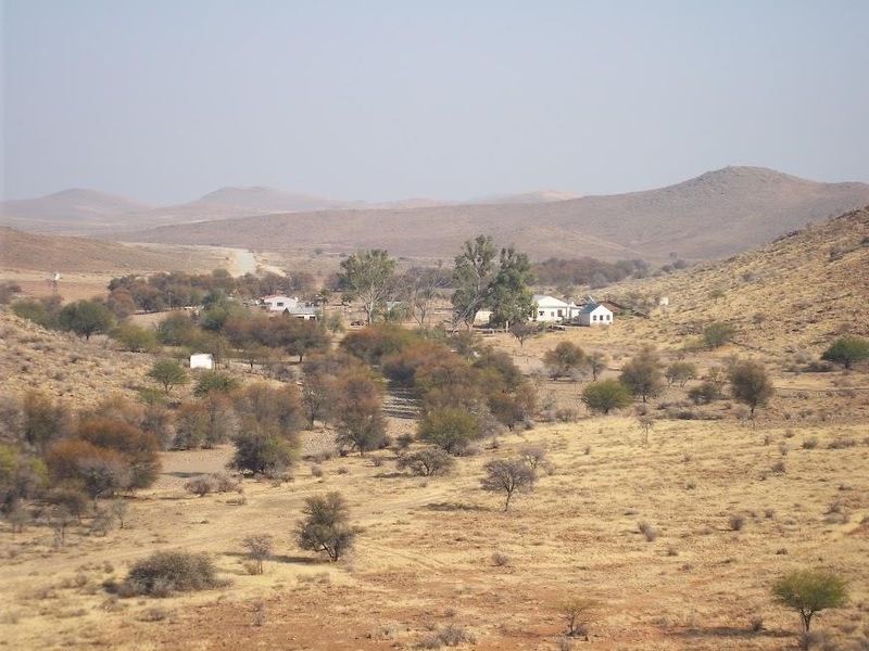 A wide-angle landscape view of the farm property, showcasing the surrounding arid terrain, hills, and scattered farm buildings in the distance.