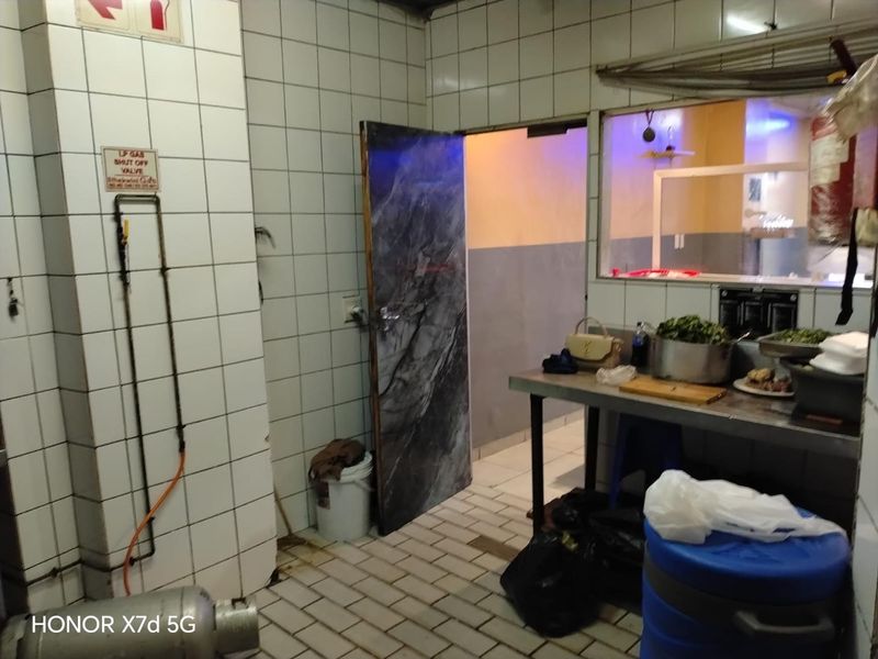 A functional commercial scullery or prep area featuring tiled walls, a service window, and gas infrastructure, requiring maintenance and cosmetic updates.
