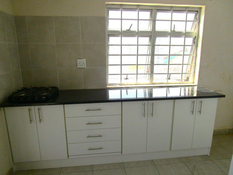 A functional kitchen area featuring white built-in cabinetry, a dark granite countertop, a gas hob, and a window with security bars.