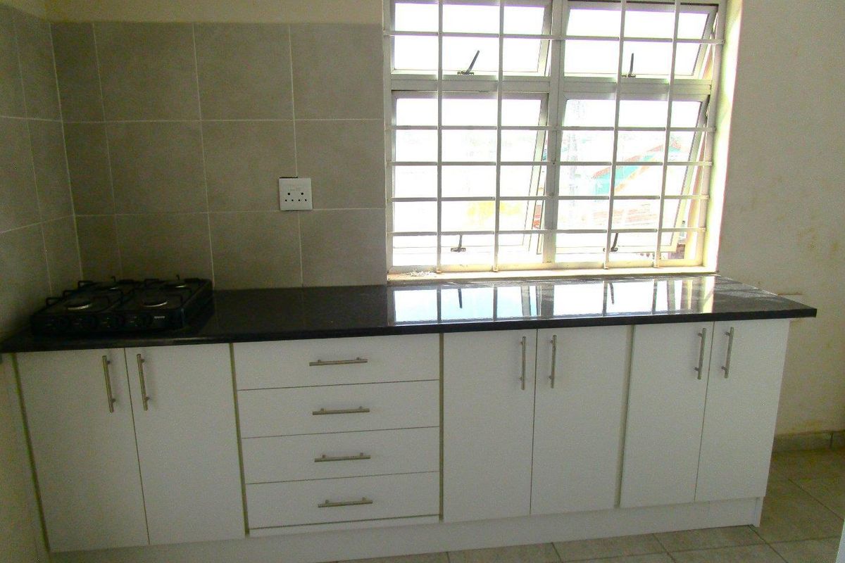 A functional kitchen area featuring white built-in cabinetry, a dark granite countertop, a gas hob, and a window with security bars.