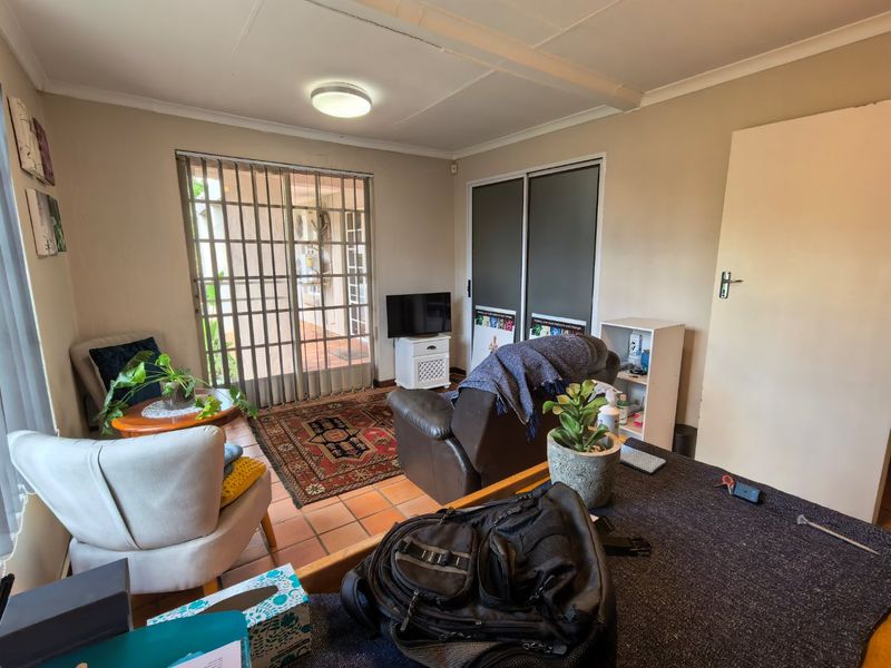 A living room featuring terracotta floor tiles, built-in cupboards, and a sliding security gate providing access to the exterior.