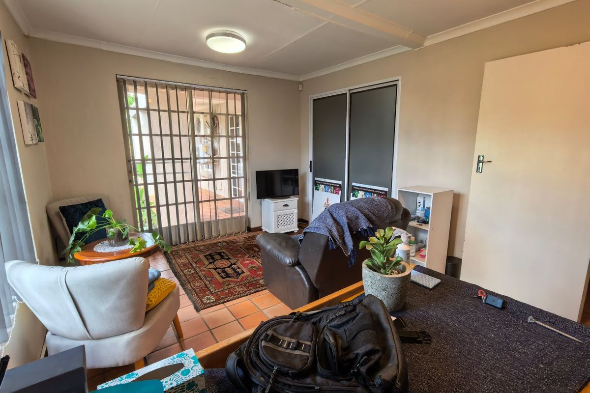 A living room featuring terracotta floor tiles, built-in cupboards, and a sliding security gate providing access to the exterior.
