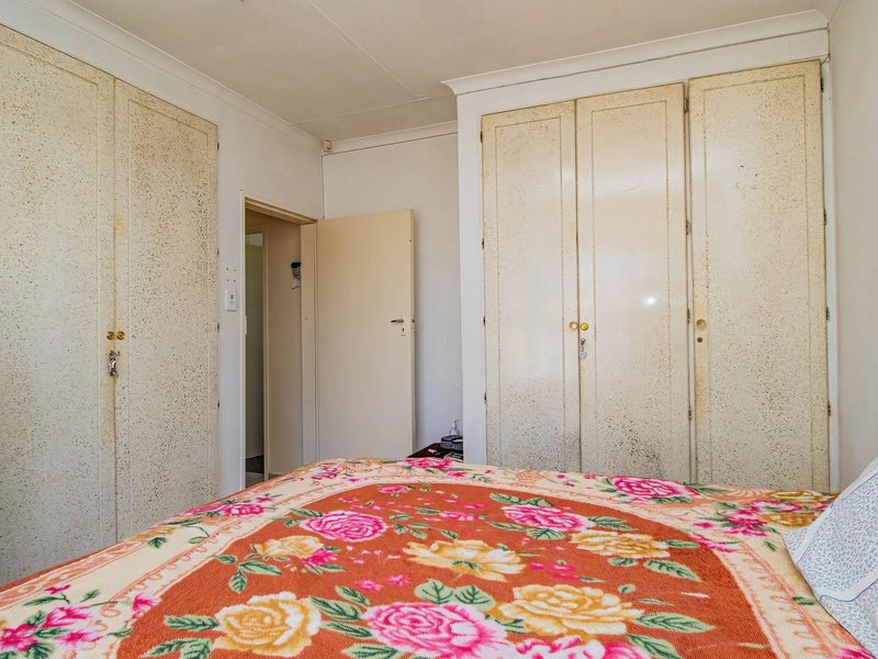 A bedroom featuring built-in cupboards with dated finishes and coved ceiling detailing.