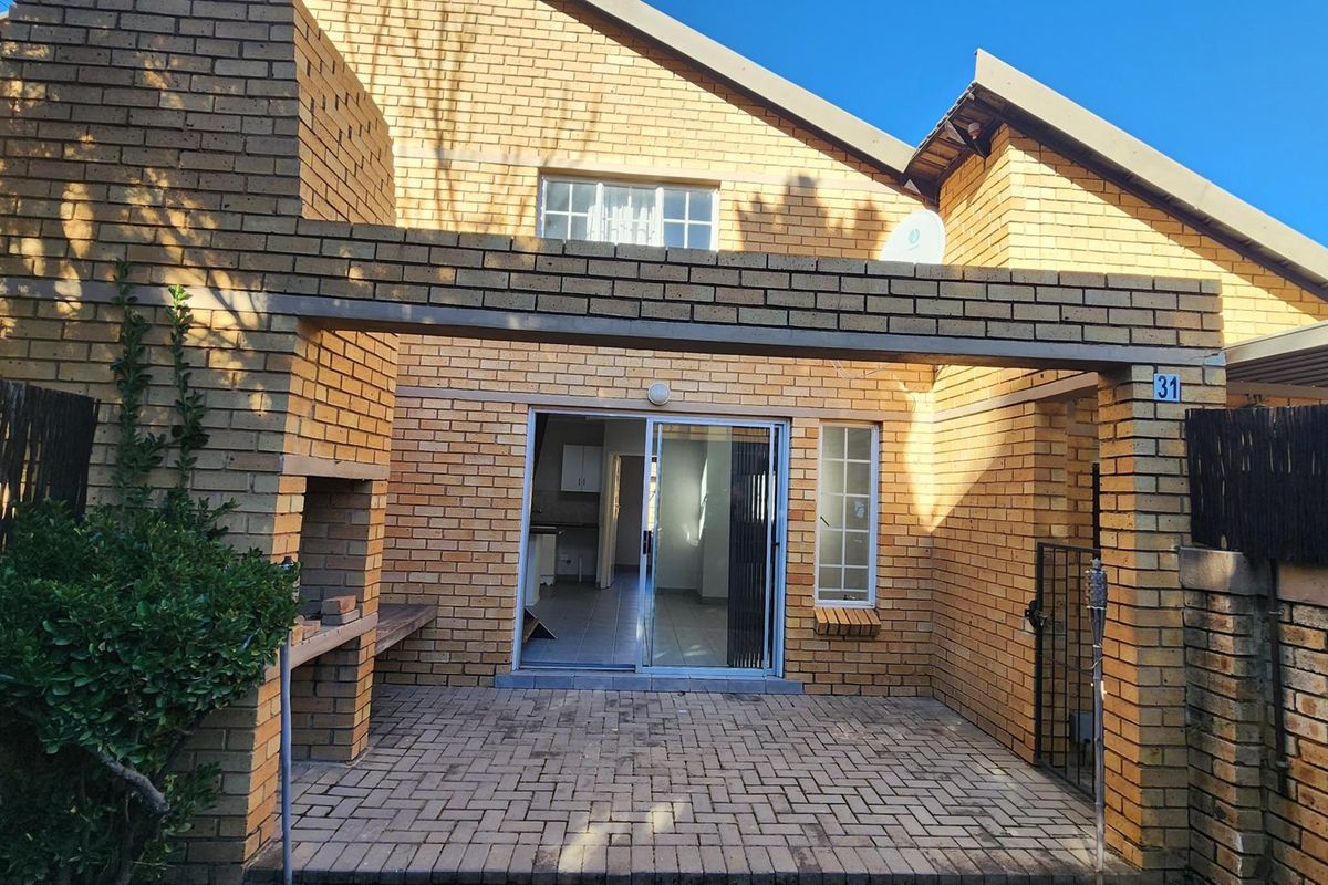 Rear exterior view featuring a brick facade, a paved patio area with a built-in braai, and sliding glass door access to the interior.