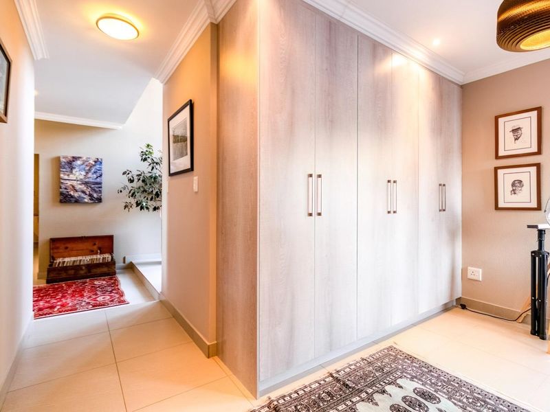 A well-maintained hallway featuring light wood-finish built-in cupboards, neutral tiled flooring, and elegant cove cornicing.