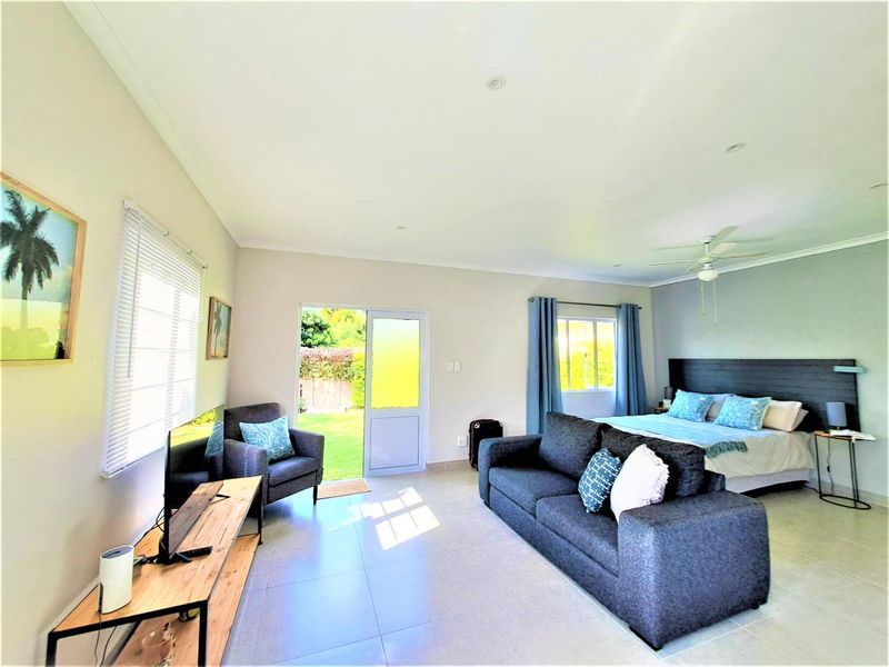 An open-plan living and bedroom area featuring tiled floors, a ceiling fan, recessed lighting, and direct access to the rear garden through a glass door.