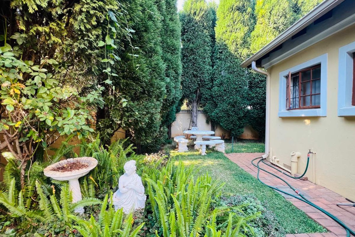 A private rear garden featuring a brick pathway, established hedges, and a small lawn area adjacent to the house exterior.