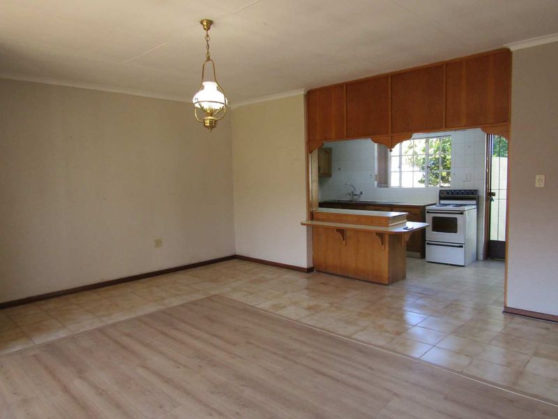 Open plan living and kitchen area featuring a breakfast bar, built-in cabinetry, and a mix of laminate and tiled flooring in a retirement village unit.