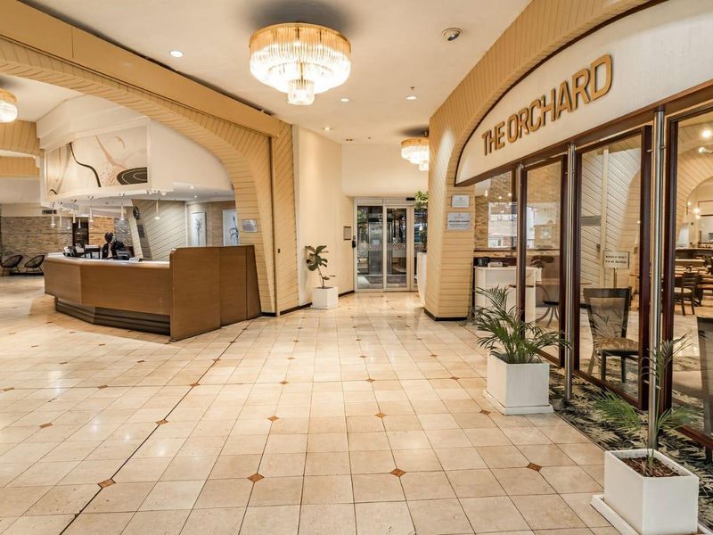A spacious, well-lit apartment complex lobby or clubhouse area featuring tiled floors, a reception desk, and elegant arched architectural elements.