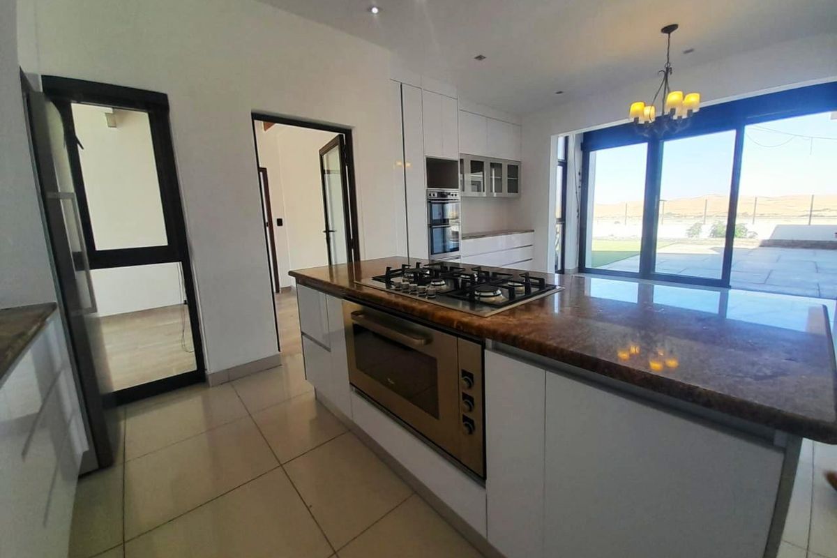 Modern open-plan kitchen featuring a central island with a built-in gas hob and oven, sleek cabinetry, and large sliding doors leading to the patio.