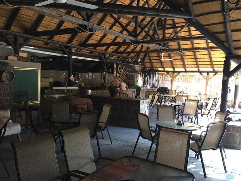 Spacious covered outdoor entertainment area featuring a high thatched roof with exposed timber trusses, a stone-clad bar counter, and built-in braai facilities.