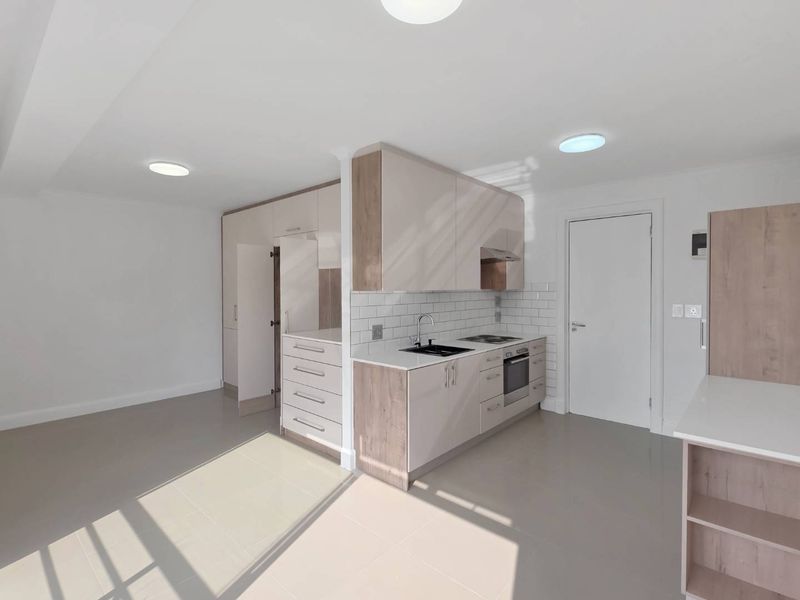 Modern open-plan kitchen featuring sleek two-tone cabinetry, subway tile backsplash, integrated appliances, and neutral tiled flooring in a bright, well-maintained space.