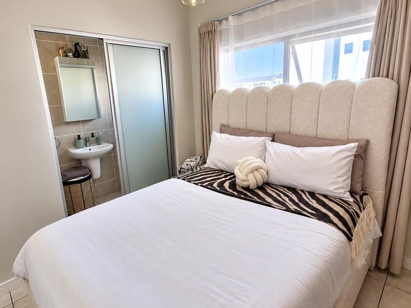 A well-maintained bedroom featuring tiled flooring, neutral tones, and an integrated en-suite bathroom with a pedestal basin and sliding door access.