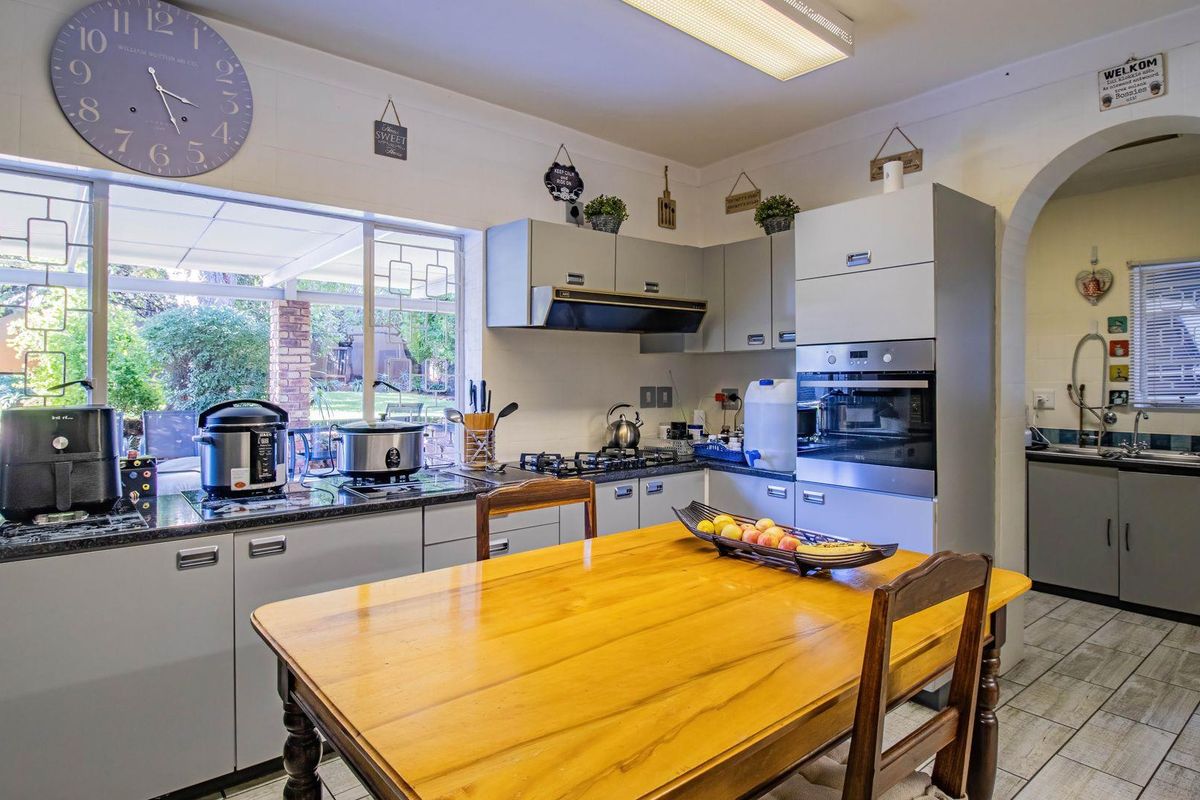 A functional kitchen featuring built-in cabinetry, integrated oven, gas hob, and extractor fan, with an adjacent scullery area visible through the archway.