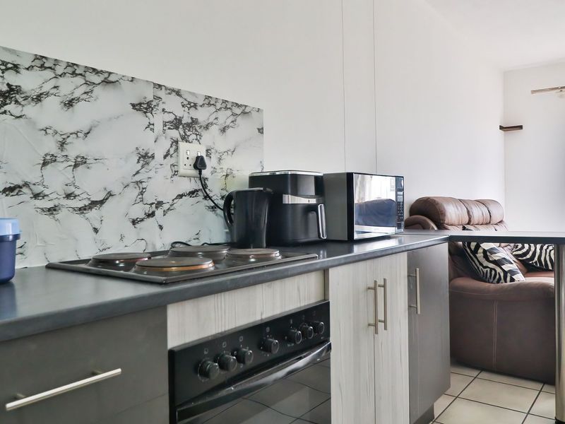 Open-plan kitchen and living area featuring modern marble-effect splashback, built-in oven, electric hob, and tiled flooring, creating a functional and connected living space.