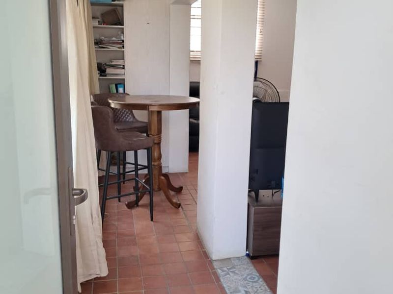 A narrow hallway featuring terracotta floor tiles and built-in shelving, connecting to adjacent living spaces through an archway.