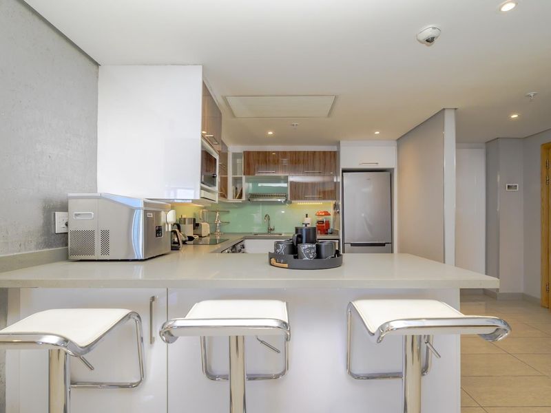 Modern kitchen featuring stone countertops, sleek cabinetry, integrated appliances, and a breakfast bar, finished with recessed lighting and neutral floor tiles.