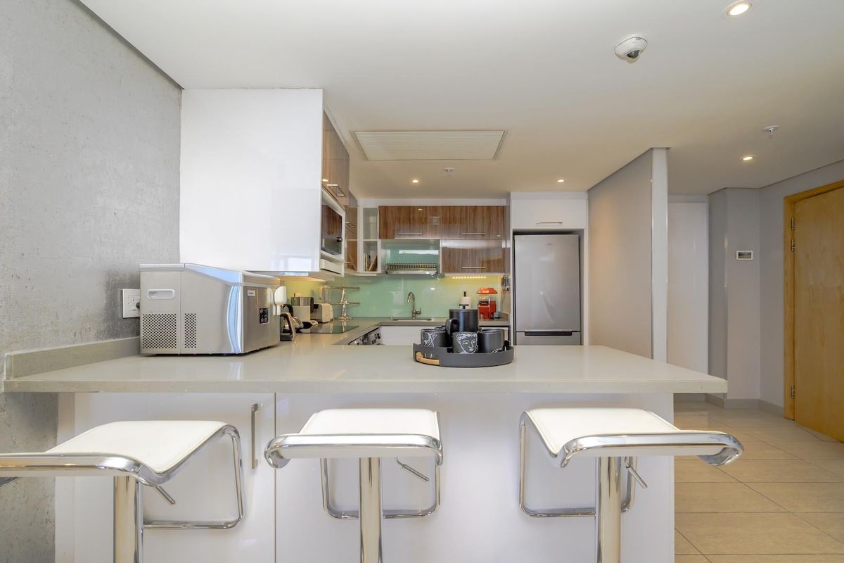 Modern kitchen featuring stone countertops, sleek cabinetry, integrated appliances, and a breakfast bar, finished with recessed lighting and neutral floor tiles.