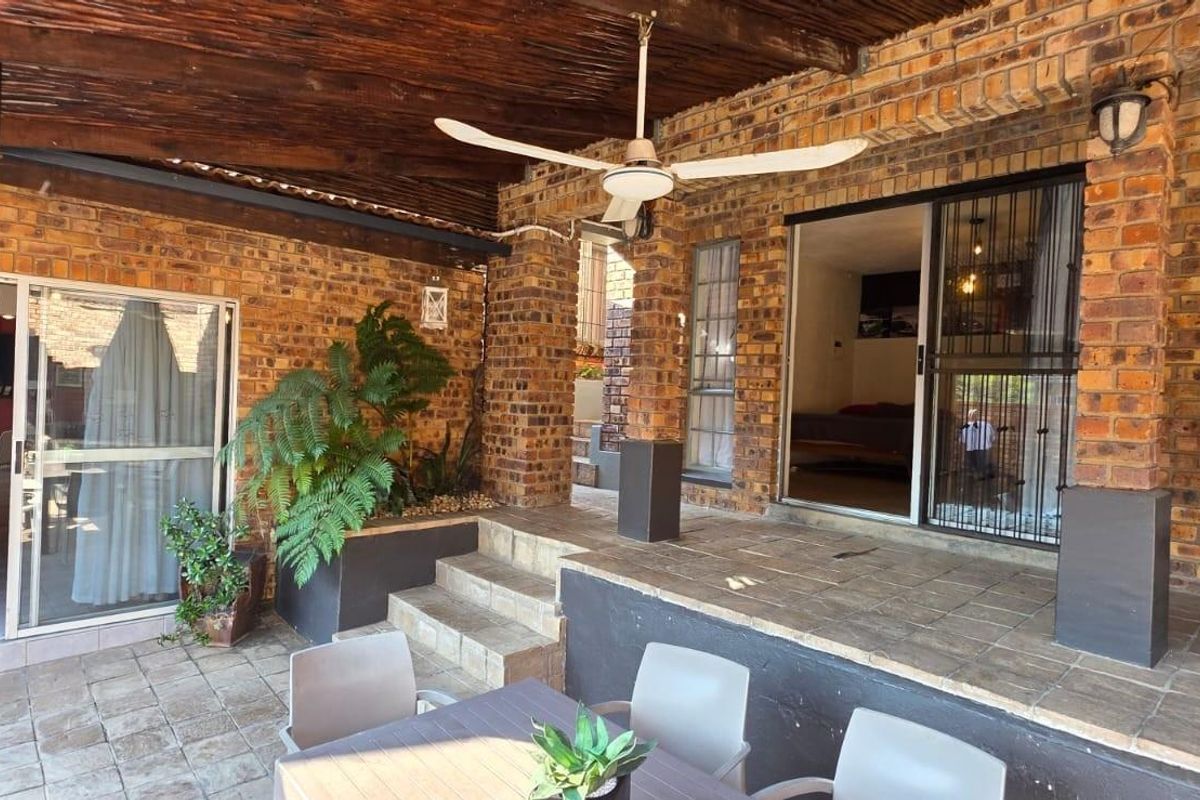 Covered patio area featuring exposed brickwork, a thatched ceiling with a fan, and direct access to the interior through sliding glass doors.