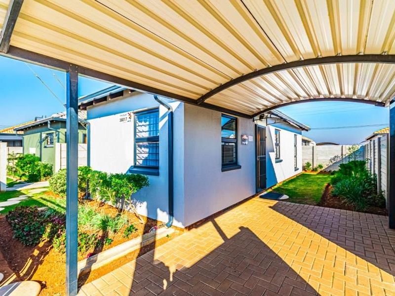 Front exterior view featuring a covered carport, paved driveway, and landscaped garden area with secure boundary walling.