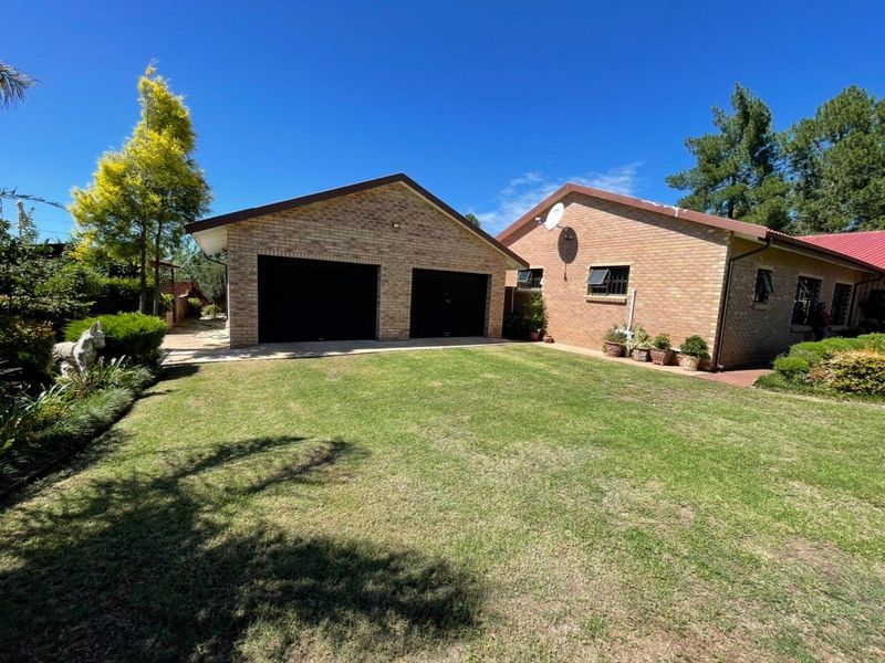 A view of the rear exterior featuring a brick double garage, well-maintained lawn, and established garden surroundings.