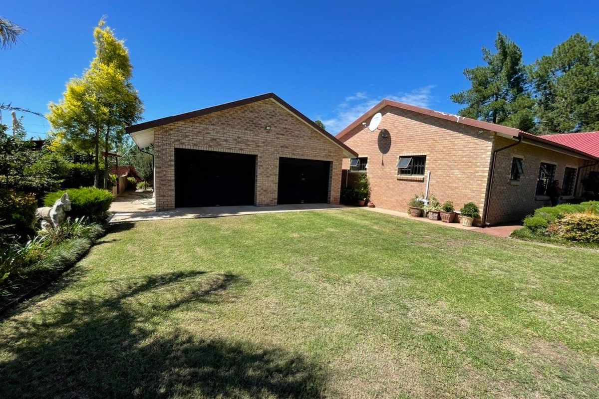 A view of the rear exterior featuring a brick double garage, well-maintained lawn, and established garden surroundings.