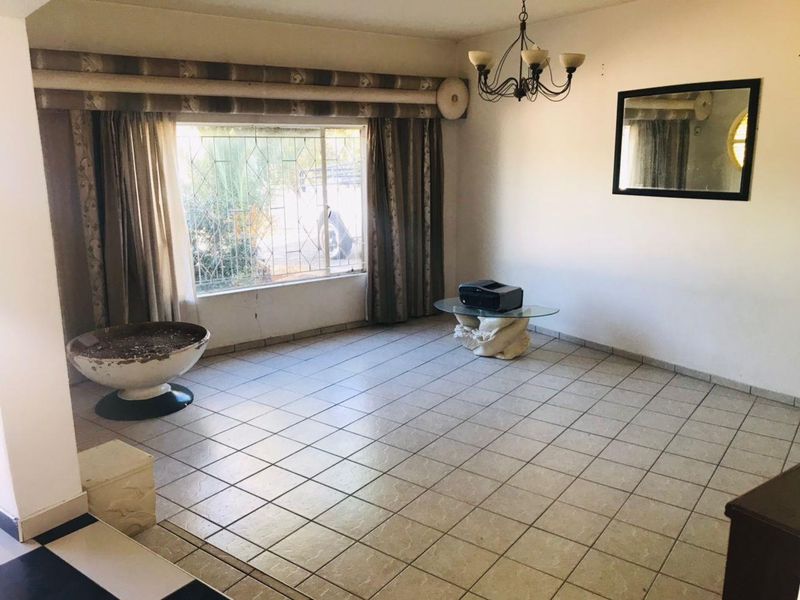 A spacious, tiled living room featuring large windows with security bars and a central ceiling light fixture, offering a blank canvas for renovation.