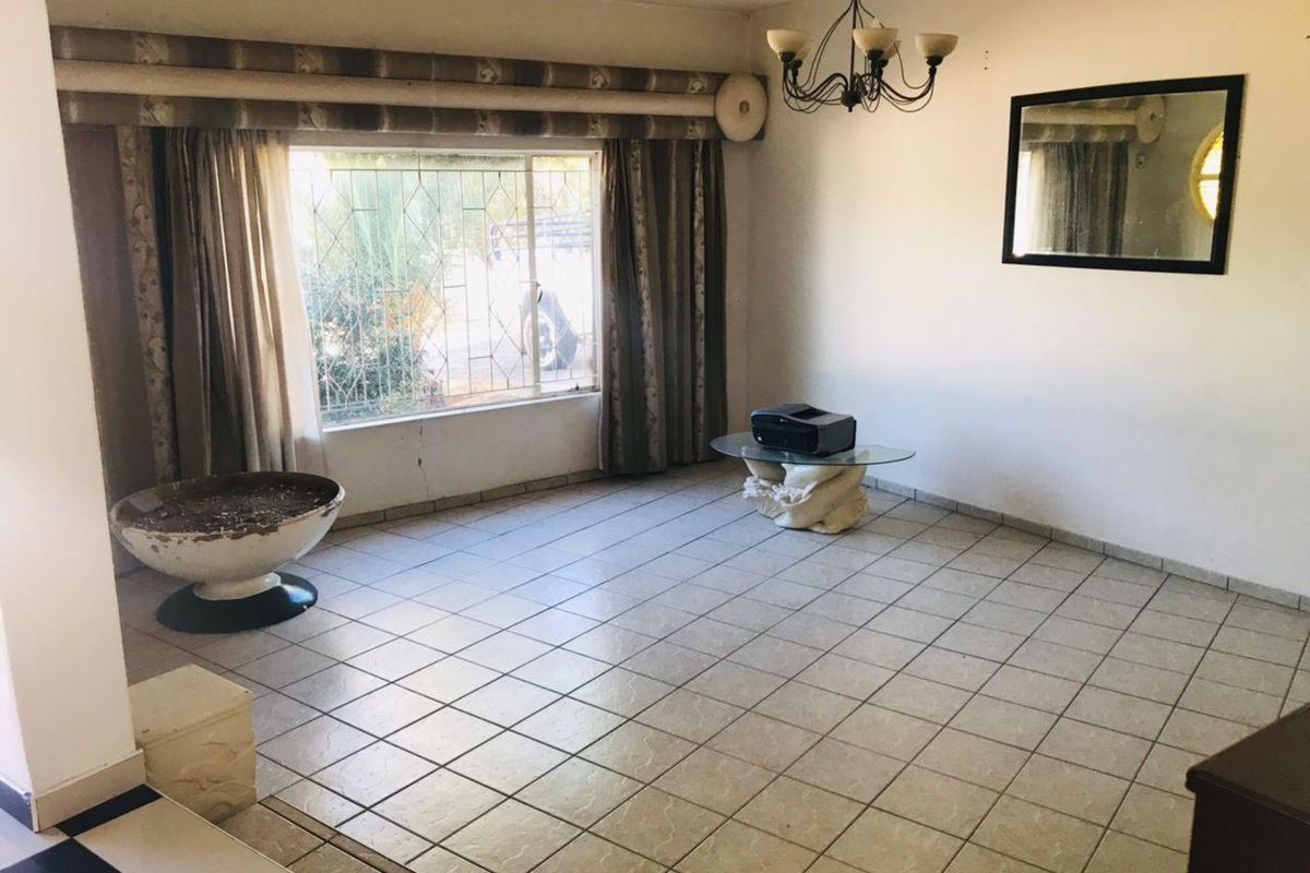 A spacious, tiled living room featuring large windows with security bars and a central ceiling light fixture, offering a blank canvas for renovation.