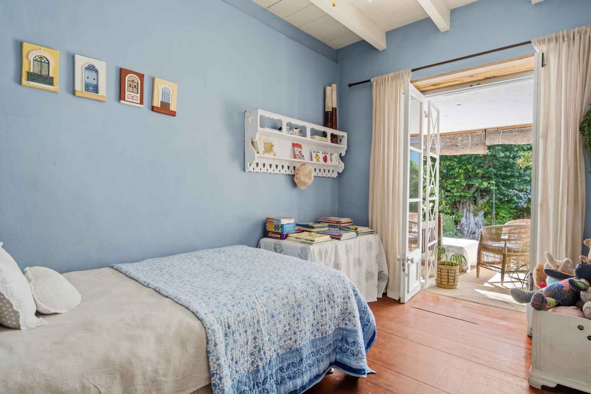 A bright bedroom featuring exposed timber ceiling beams, warm timber flooring, and double french doors opening onto a private patio area.