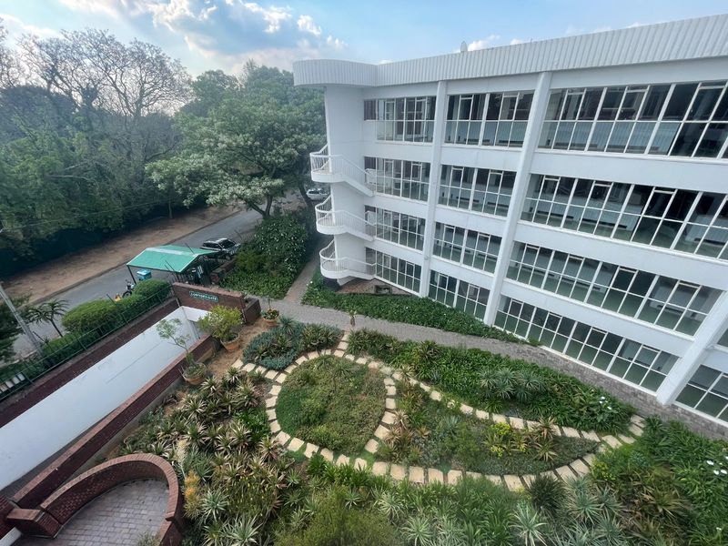 Aerial view of the apartment complex featuring a well-maintained landscaped garden, paved walkways, and external stairwell access.