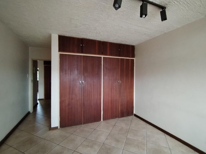 An empty bedroom featuring built-in wooden cupboards, tiled flooring, and overhead track lighting, offering a blank canvas for potential updates.