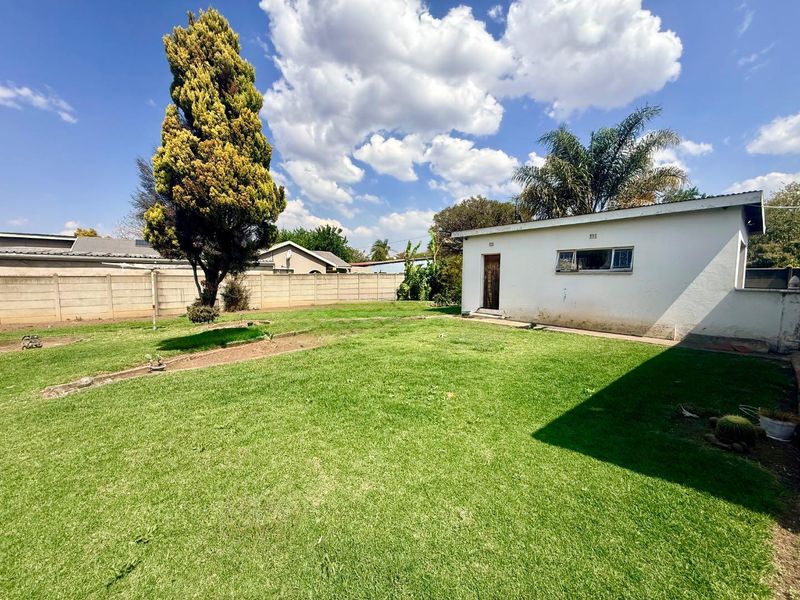 A spacious rear garden featuring a large lawn, mature trees, and a detached outbuilding with a precast concrete boundary wall.
