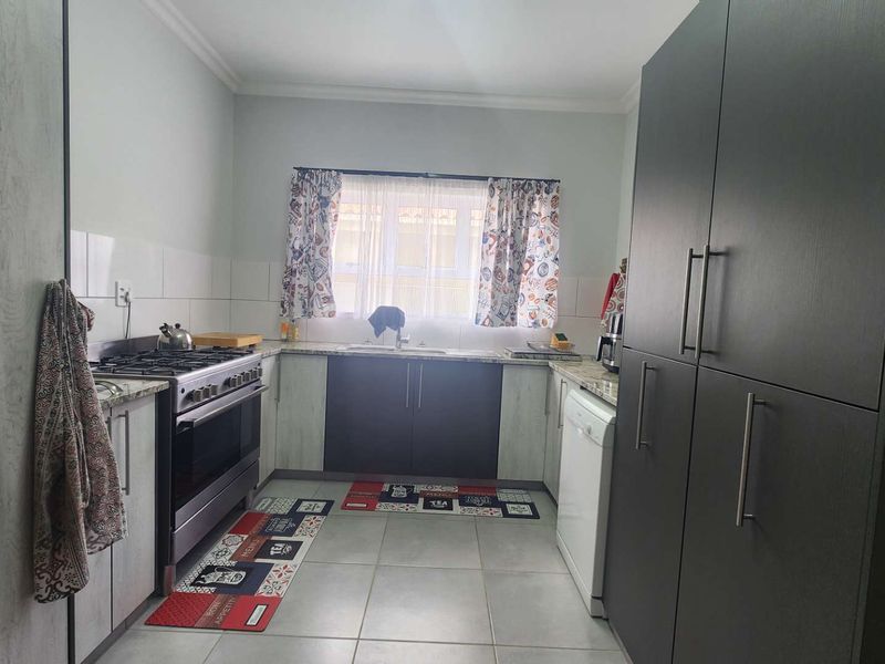 A functional kitchen featuring dark and light cabinetry, granite countertops, a gas stove, and tiled flooring with a window overlooking the exterior.