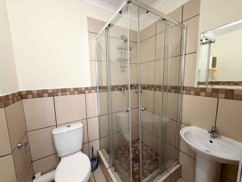 A functional bathroom featuring a glass shower enclosure, pedestal basin, and toilet with neutral wall and floor tiling.