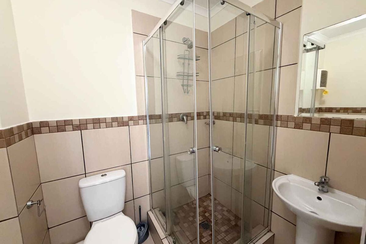 A functional bathroom featuring a glass shower enclosure, pedestal basin, and toilet with neutral wall and floor tiling.