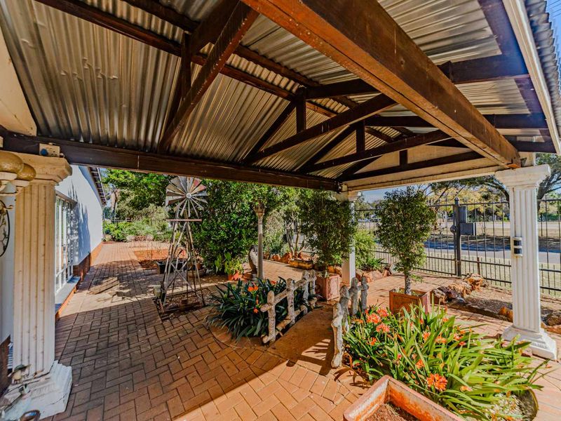 A covered outdoor patio area featuring a corrugated metal roof, timber support beams, and decorative columns, overlooking a landscaped garden space.