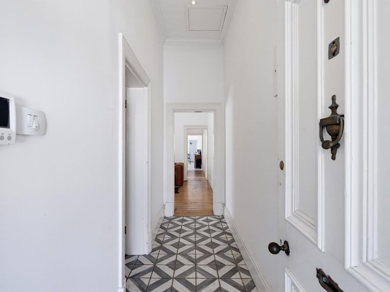 A bright, clean hallway featuring patterned floor tiles, timber flooring in the adjoining rooms, and a security alarm system.