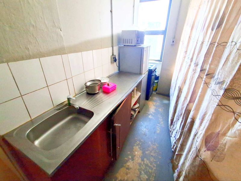 A compact kitchen area featuring a stainless steel sink, tiled splashback, and basic cabinetry, currently showing signs of significant wear and tear.