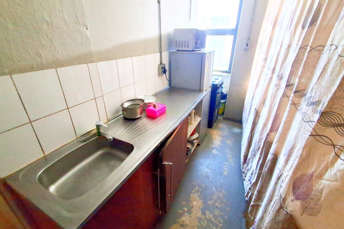A compact kitchen area featuring a stainless steel sink, tiled splashback, and basic cabinetry, currently showing signs of significant wear and tear.