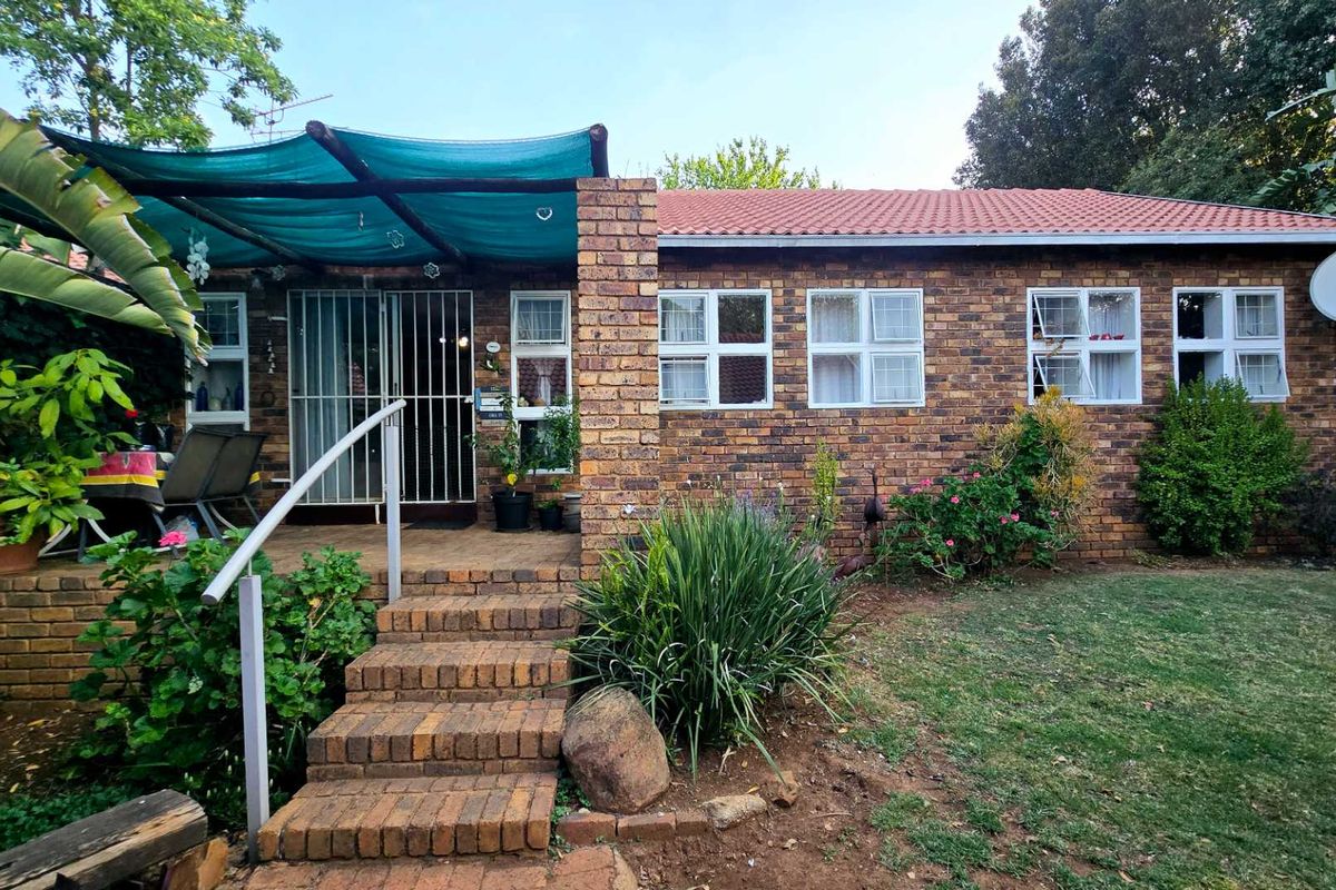 Rear view of a face brick townhouse featuring a covered patio area, brick staircase, and a small garden space.