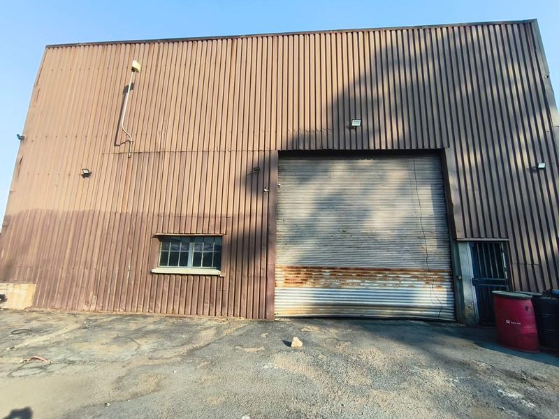 Industrial building exterior featuring corrugated metal cladding, a large roller shutter door, and an asphalt driveway area.