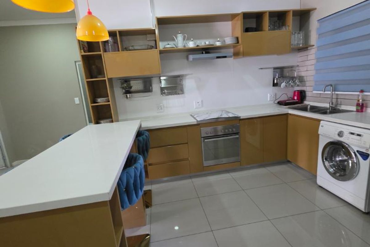 Modern kitchen featuring light wood cabinetry, stone countertops, built-in oven, extractor fan, and a breakfast bar with integrated laundry appliance space.