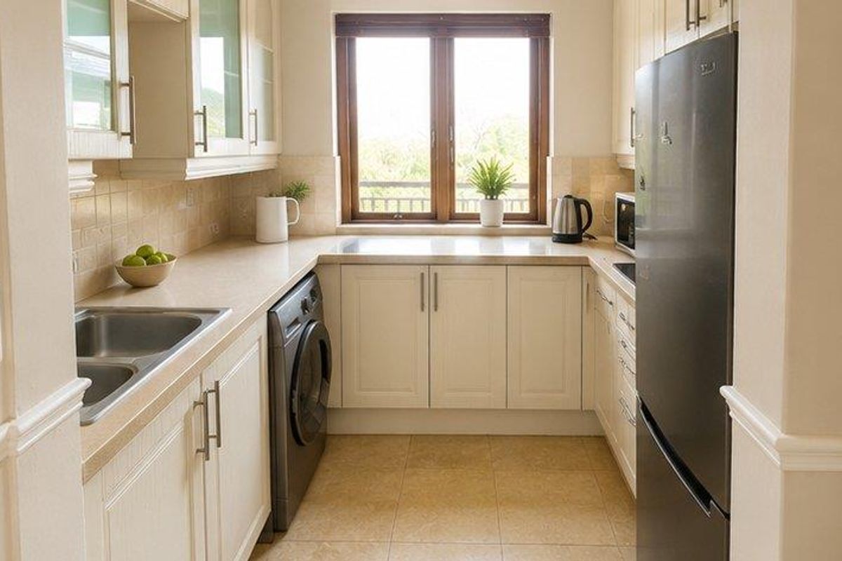 A functional kitchen featuring cream-colored cabinetry, laminate countertops, a double stainless steel sink, and tiled flooring with a window providing natural light.